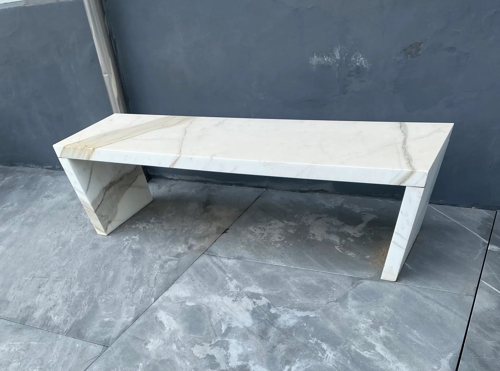 A minimalist bench in Calacatta Gold marble with angled, mitred legs.