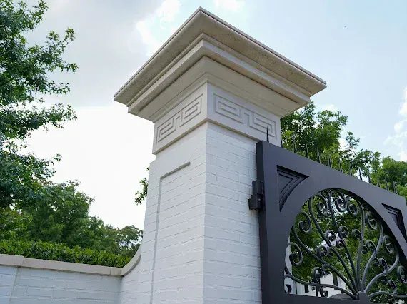 A stepped limestone pier cap with a carved Greek key frieze, crowning an entry gate pillar.