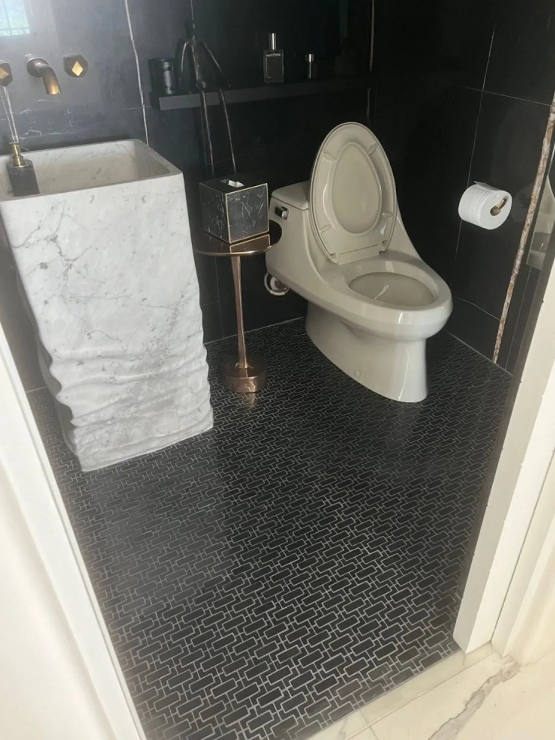 The carved marble pedestal sink set against black marble walls and a black mosaic floor.