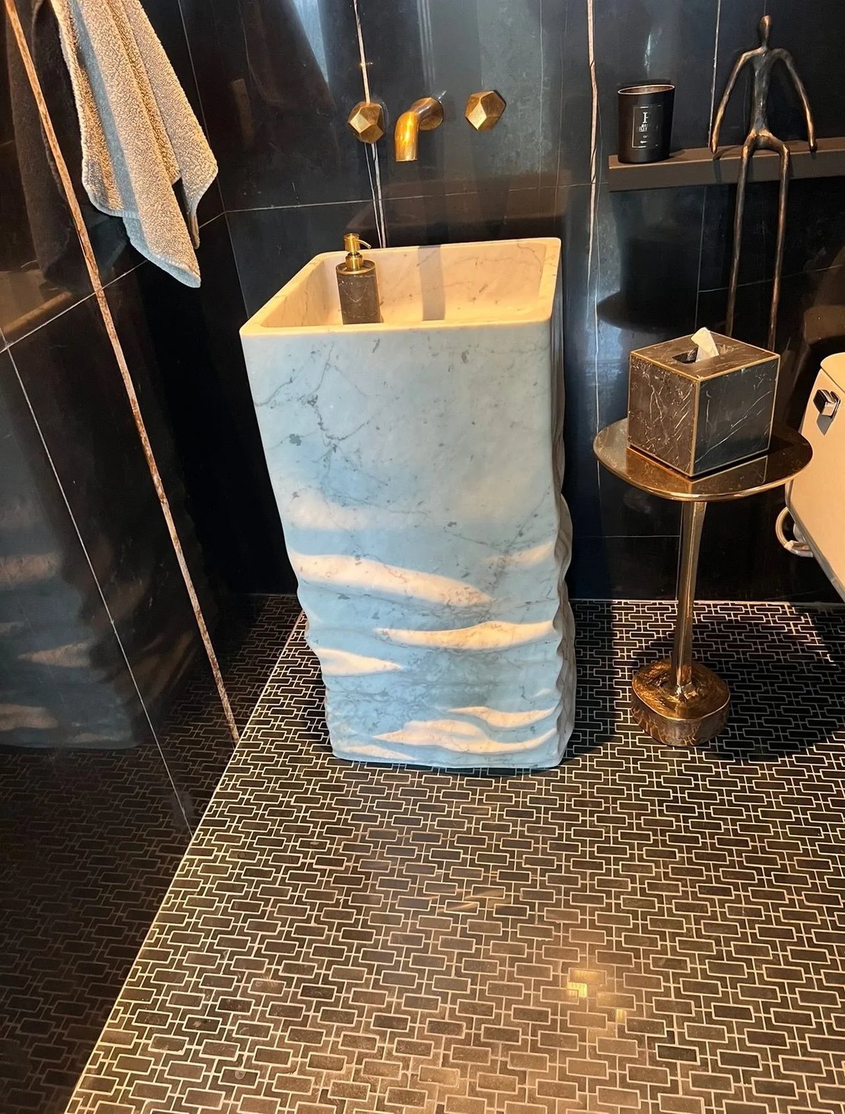 A monolithic marble pedestal sink with a rippled, hand-carved finish.