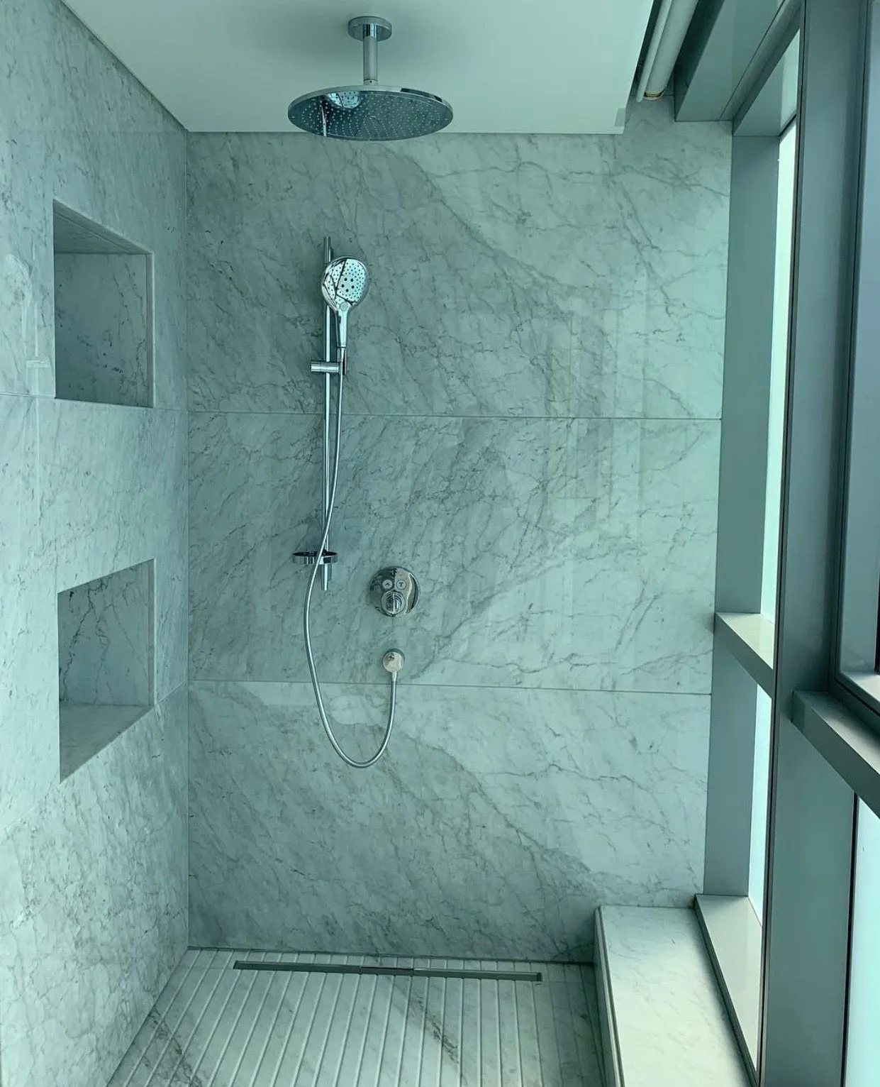 Large-format Carrara marble walls, recessed niches, a marble bench and a fluted marble floor.
