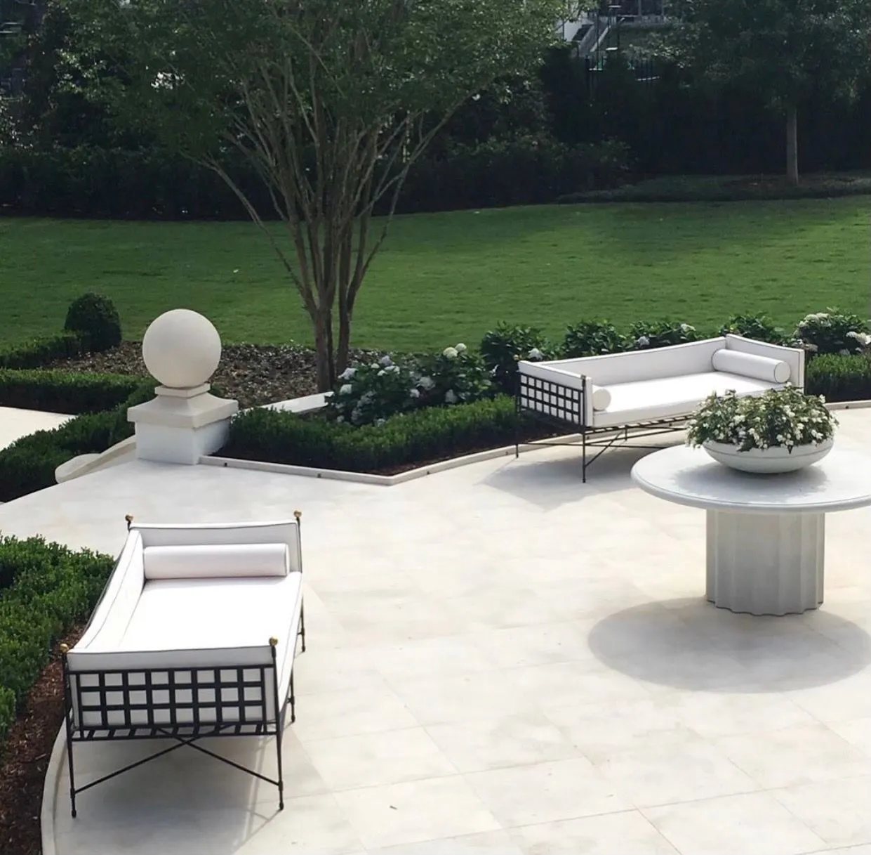A smooth limestone terrace with carved stone sphere finial, edged by formal boxwood gardens.