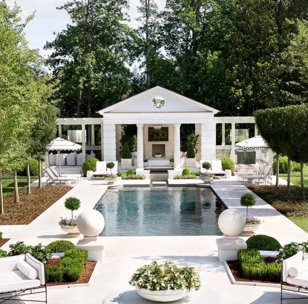 Pale limestone decking, coping and stone spheres surround a classical pool pavilion.