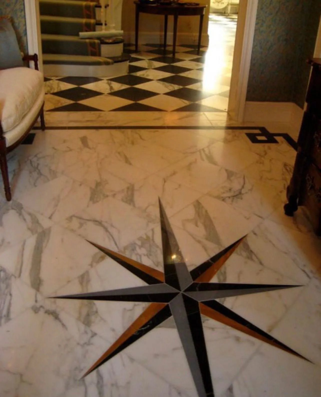 A Calacatta marble foyer with an eight-point star inlay and a black-and-white checkerboard beyond.