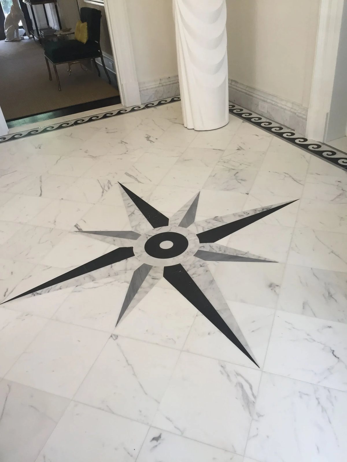 A waterjet compass rose in black, grey and white marble, bordered by a Greek wave motif.