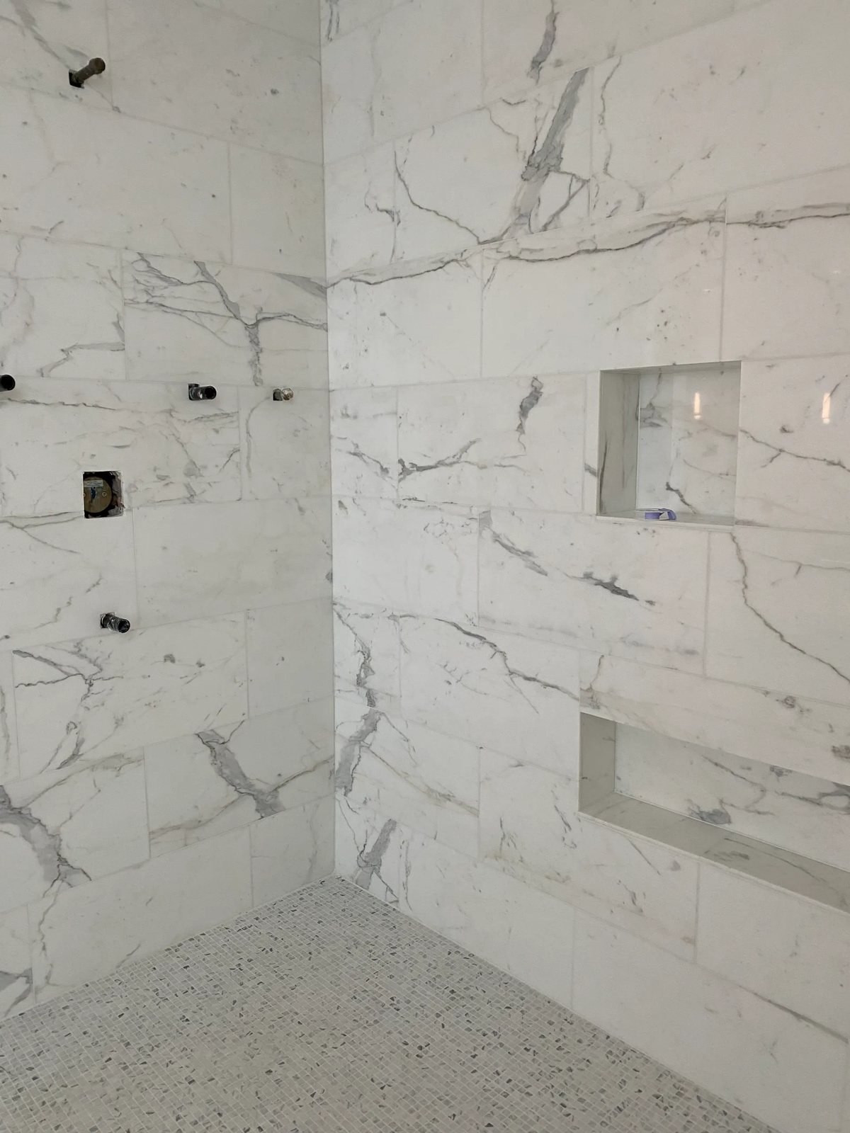 Large-format veined marble walls with recessed niches and a marble mosaic shower floor.