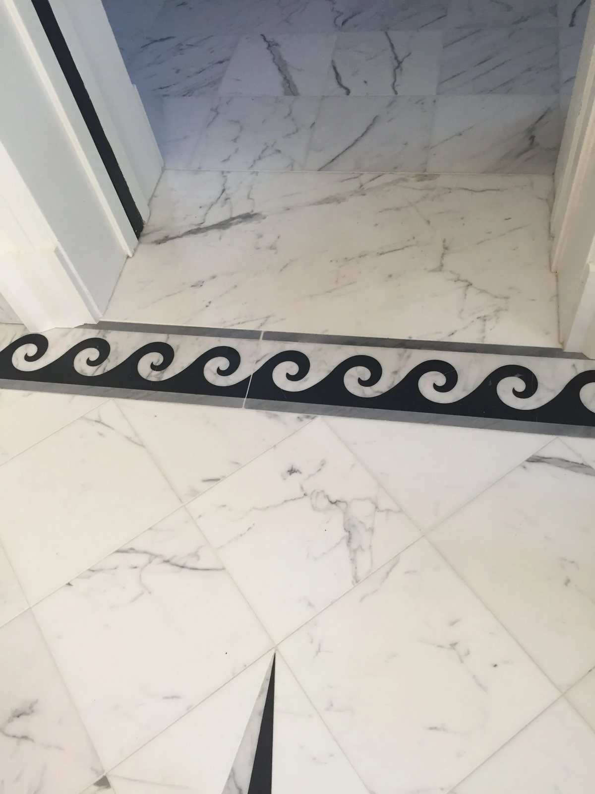 A black-and-white marble wave border with grey marble banding at a doorway threshold.