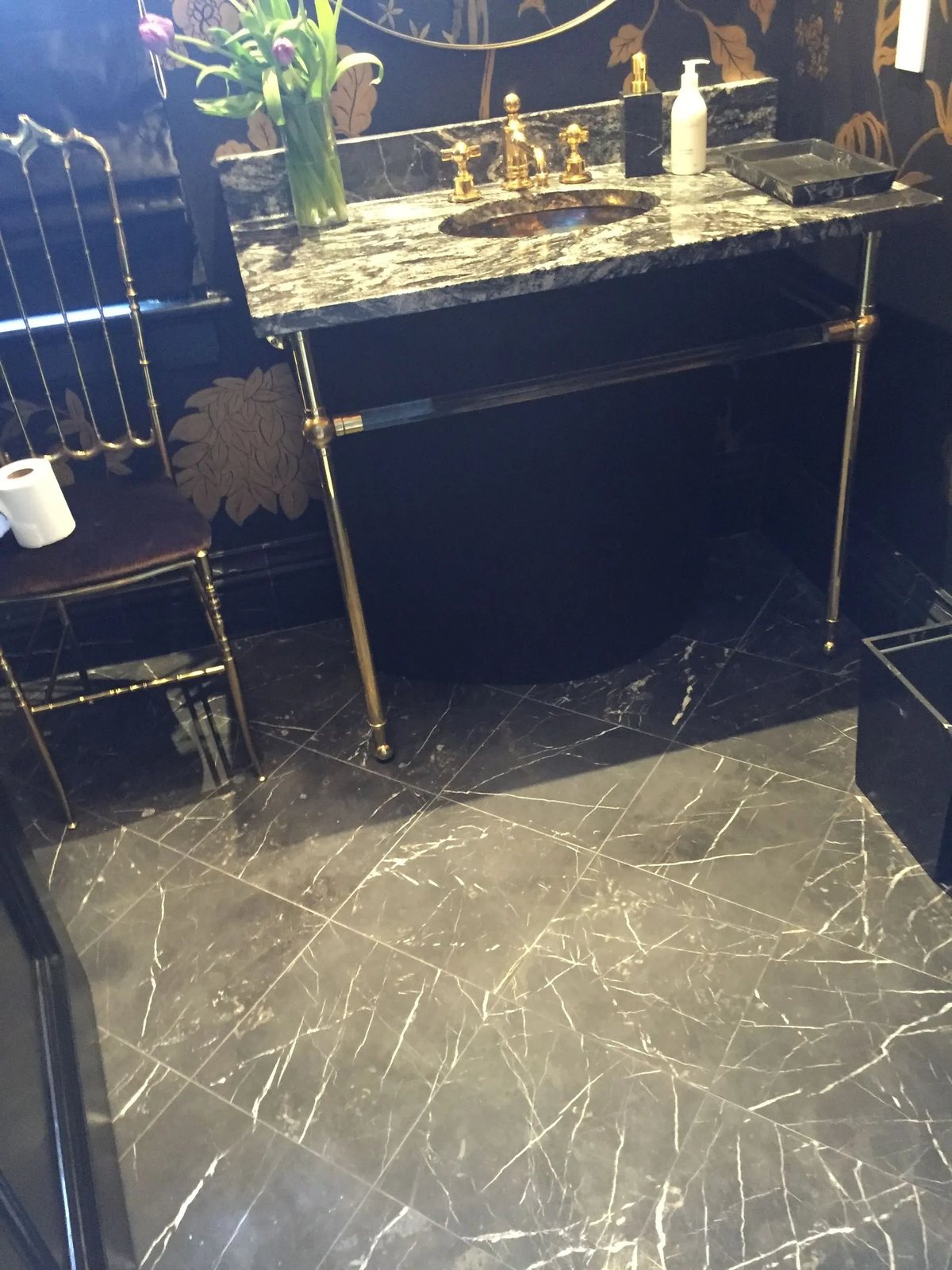 Black Nero Marquina marble flooring beneath a granite console vanity with brass fittings.