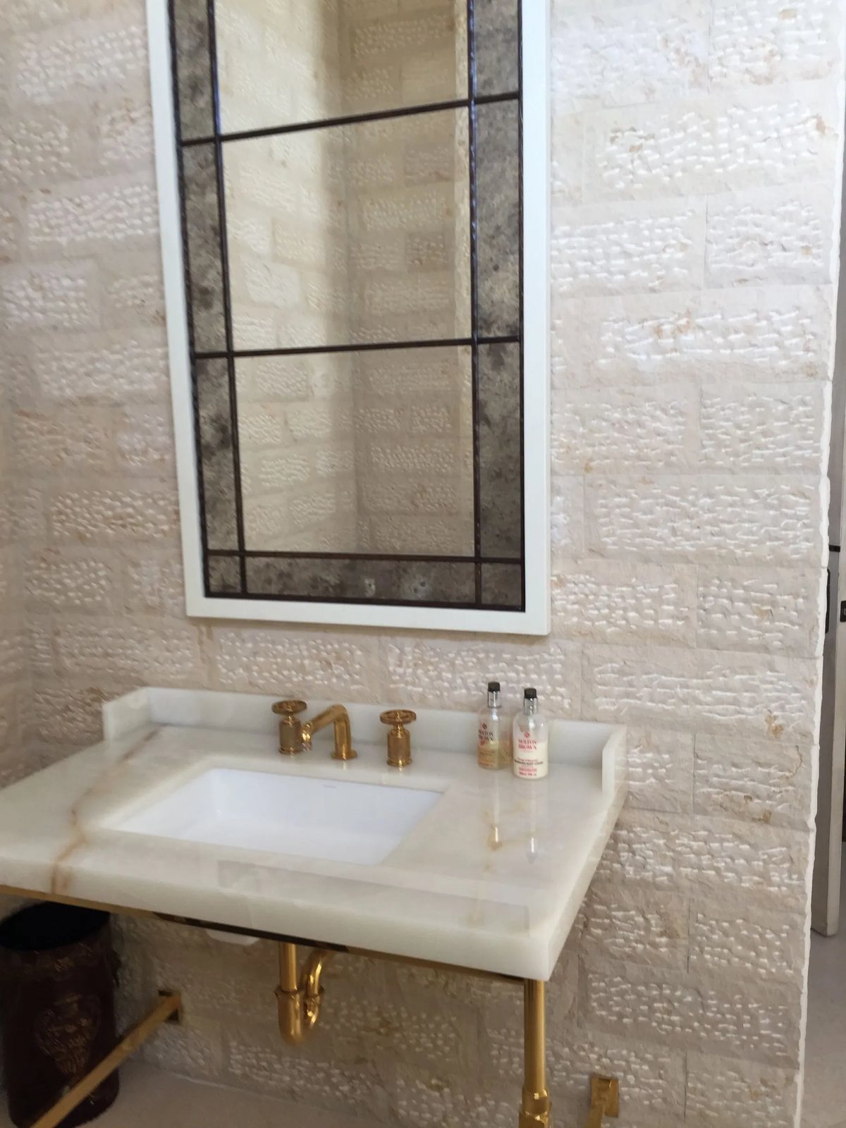 A honey-veined white onyx vanity top set against hand-chiseled limestone wall tiles.